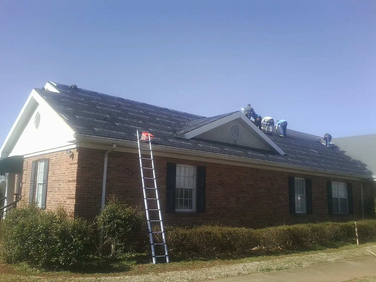 Crew tearing shingles off a brick ranch roof with a ladder set — Metal Roof Repair work by our crew in Pray
