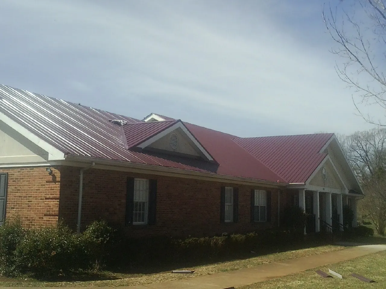 Red metal roof with gabled entries on a long brick building, from a Hail Damage Roof Repair job in Pray