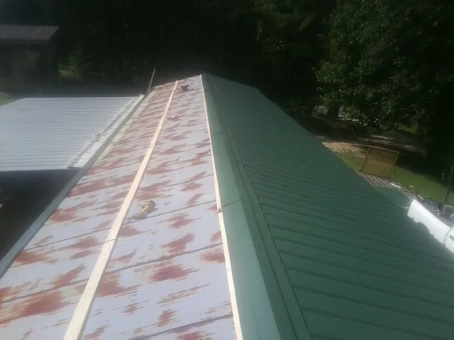 Old rusted panels beside newly installed green metal roofing — Wind Damage Roof Repair by Roofing Brothers in Pray