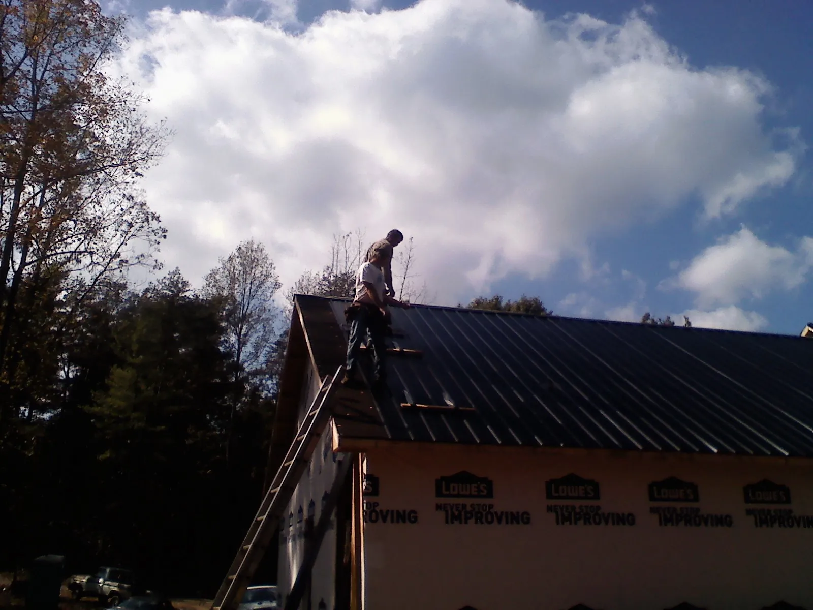 Roofer fastening dark metal panels high against a cloudy sky, from a Roof Inspection job in Pray