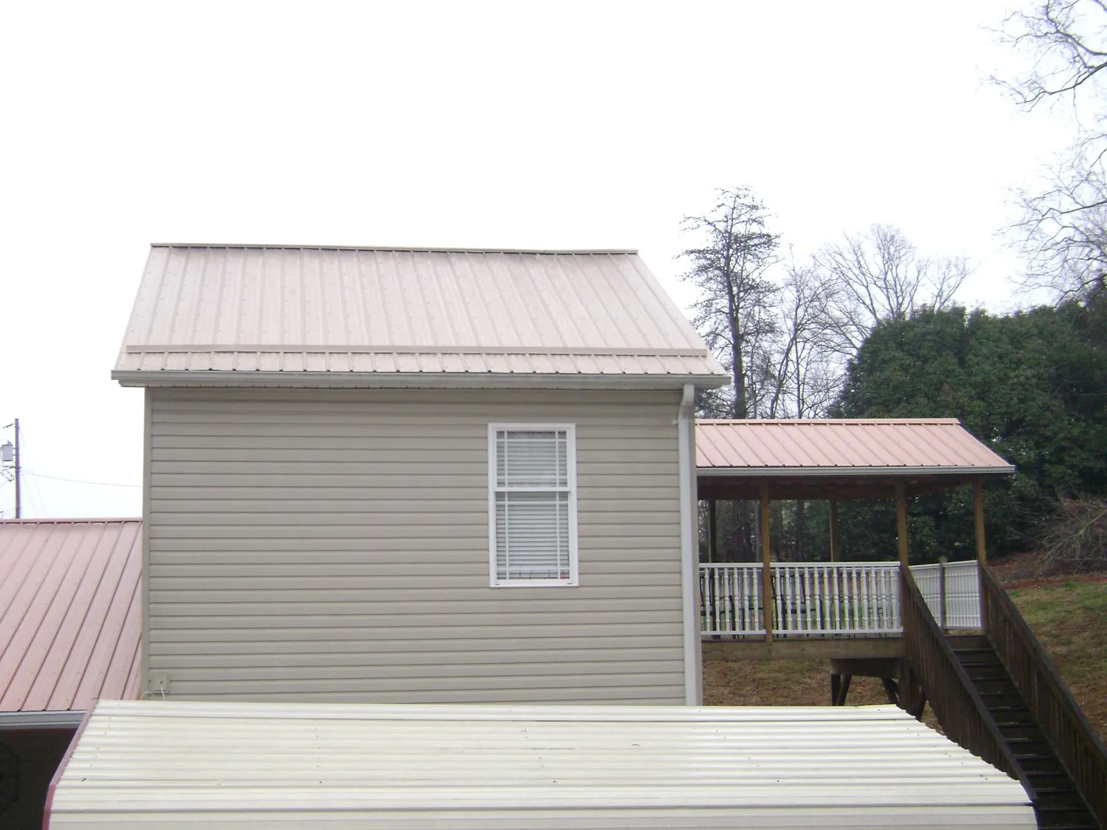 Tan metal roofs on a two story addition and attached porch, from a Roof Replacement job in Pray